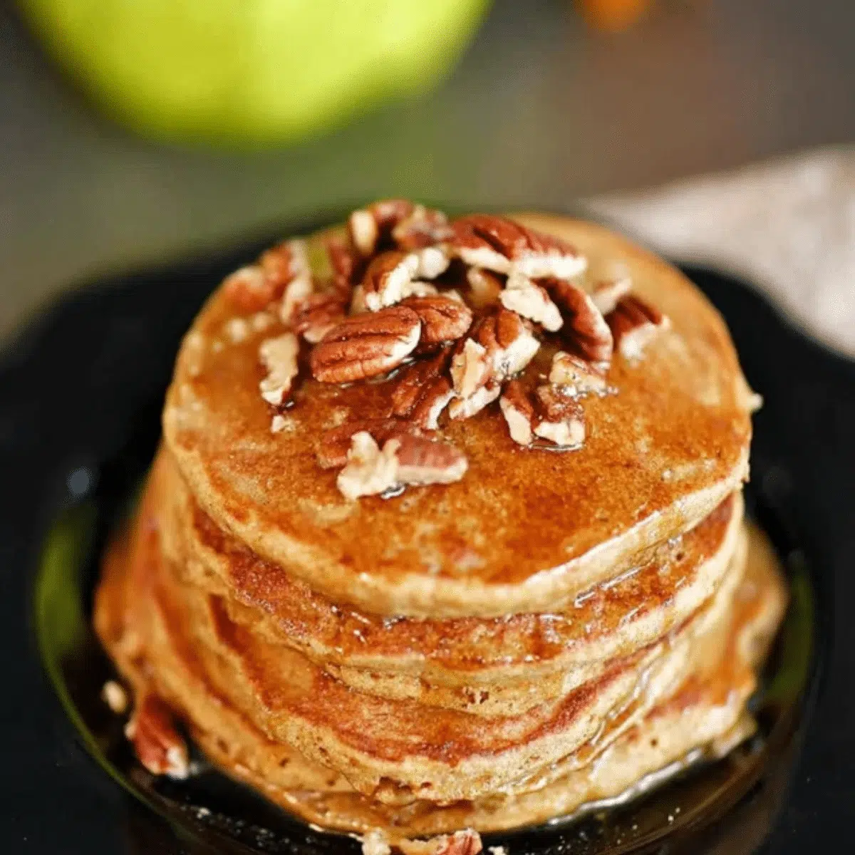 Fluffy apple butter pancakes drizzled with syrup and garnished with fresh apple slices.