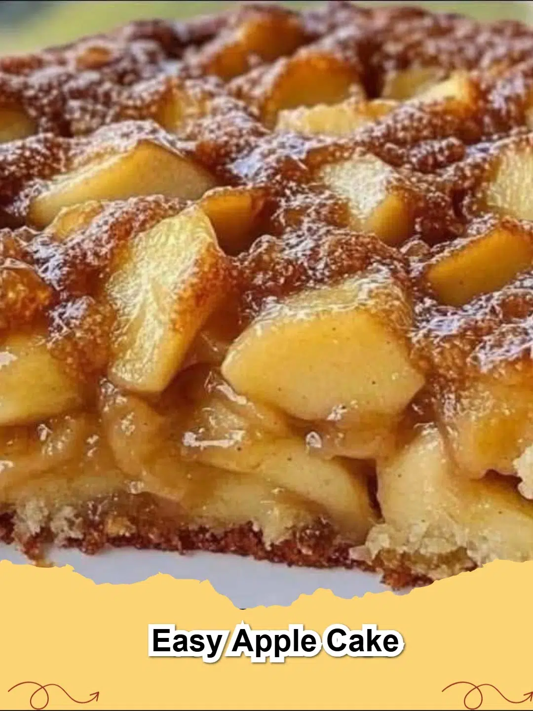 Close-up of a slice of moist Easy Apple Cake on a plate, dusted with powdered sugar, with whole apples in the background.