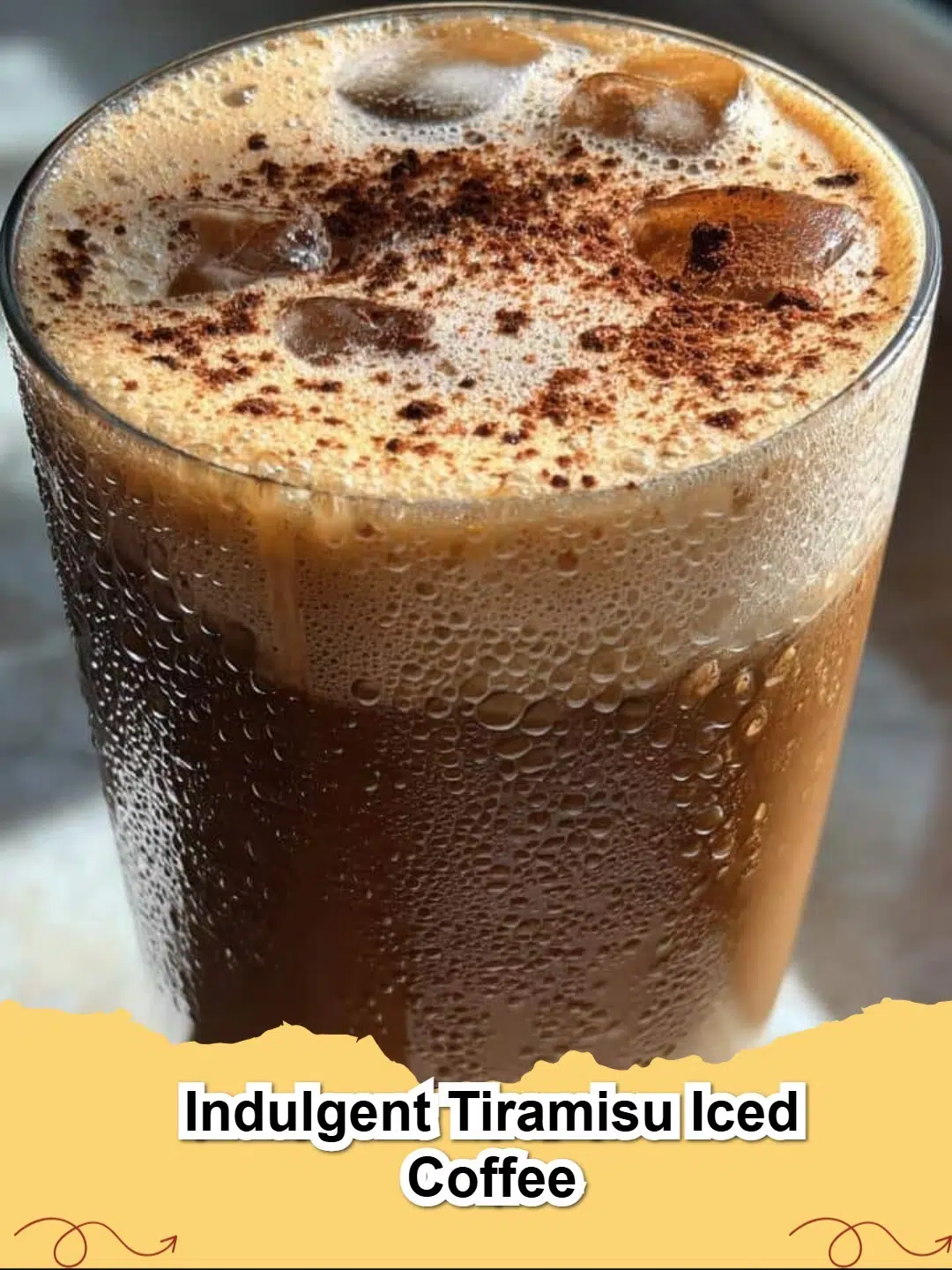 A tall glass of Indulgent Tiramisu Iced Coffee, topped with creamy mascarpone foam and dusted with cocoa powder, a perfect blend of dessert and drink.