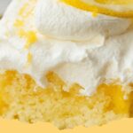A square-cut slice of delicious Lemon Poke Cake topped with white whipped cream and a twist of lemon zest.