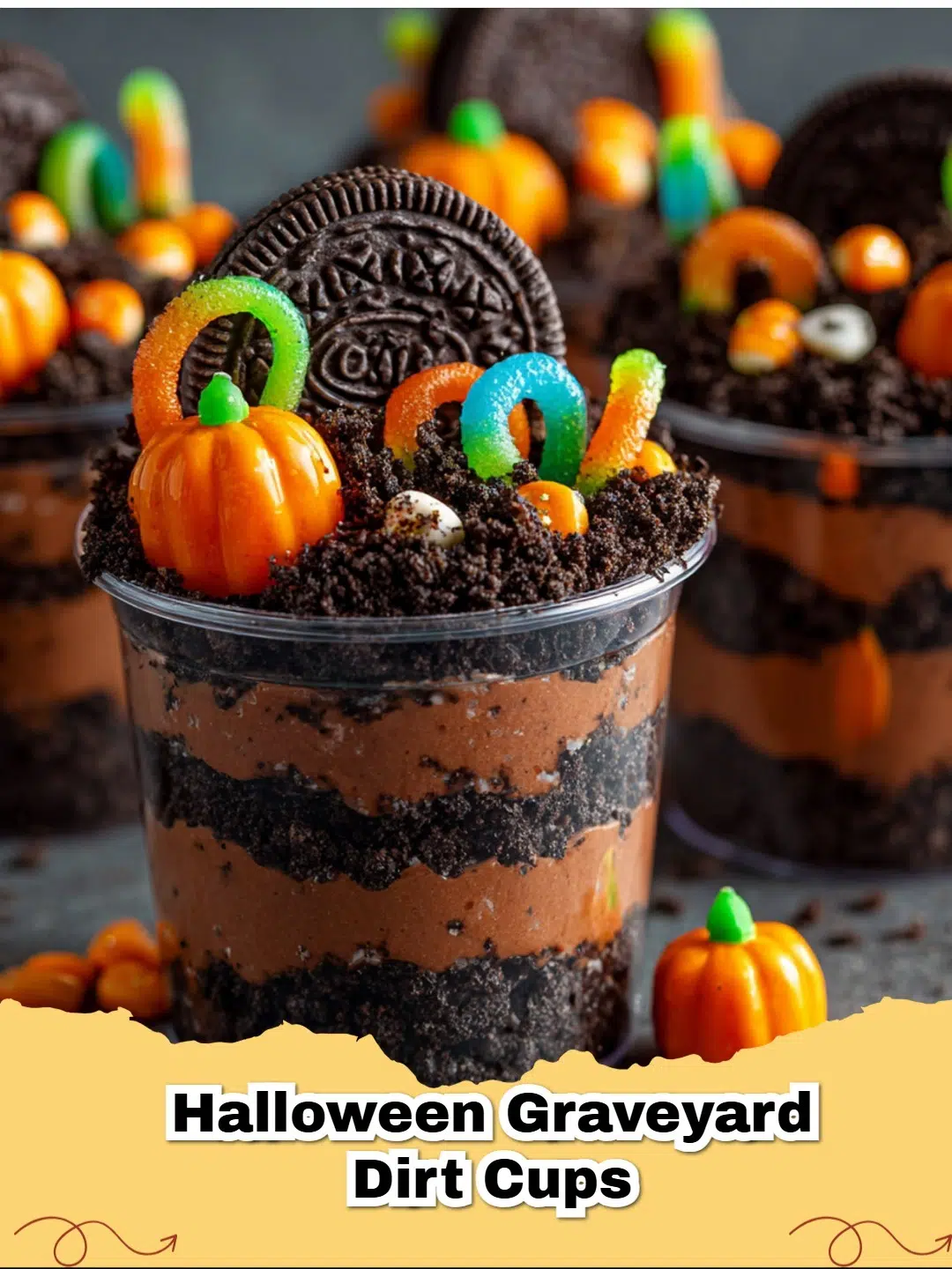 Spooky Halloween Graveyard Dirt Cups topped with gummy worms and candy pumpkins on a dark background, perfect for a Halloween party.