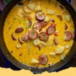 A steaming bowl of creamy Cajun Potato Soup with slices of Andouille sausage and fresh green garnish.