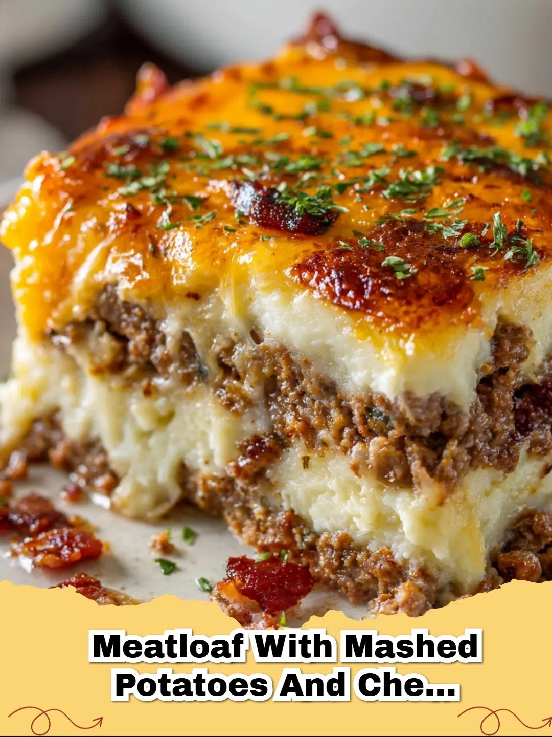 Classic Meatloaf with Mashed Potatoes and Cheese, topped with melted cheddar, served on a white plate with green garnish.