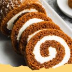 A perfectly sliced pumpkin roll with creamy white frosting and a dusting of powdered sugar, set against a rustic autumn background.