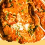 A close-up shot of a bowl of creamy lasagna soup garnished with fresh basil, mozzarella, and ricotta cheese, showing the noodles and ground beef.