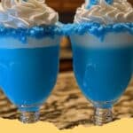 A vibrant blue Drunken Papa Smurf cocktail garnished with a cherry and lemon slice in a tall glass.
