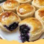 Golden-brown Blueberry Pie Bombs with a dollop of cream cheese glaze, fresh blueberries, and a dusting of powdered sugar.