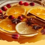 A steaming mug of Punch de Noël garnished with orange slices, cinnamon sticks, and star anise, on a festive wooden background.