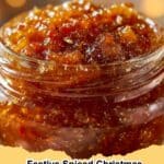 Close-up of vibrant red Festive Spiced Christmas Jam in a clear canning jar, adorned with a festive ribbon and surrounded by cinnamon sticks and star anise.