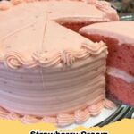 Close-up of a slice of moist Strawberry Jell-O Cake with pink cake layers and white cream cheese frosting, garnished with fresh strawberries.