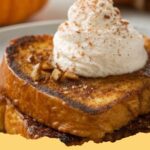 Plates of golden pumpkin brioche French toast topped with whipped cream, powdered sugar, and a drizzle of maple syrup, garnished with cinnamon sticks.