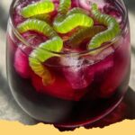 Vibrant purple Witch's Potion Punch in a large glass punch bowl with gummy worms and a spooky foggy effect from dry ice.