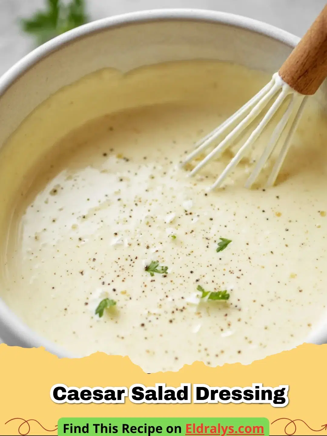 A close-up shot of a creamy Caesar Salad Dressing Recipe in a small glass jar with a whisk and lemon slice.