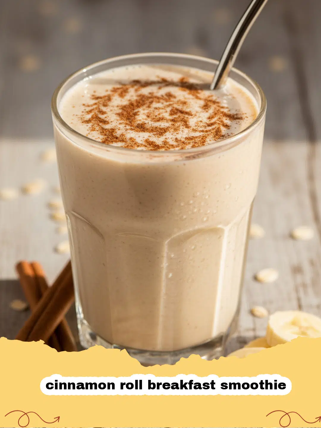 Close-up of a creamy cinnamon roll breakfast smoothie in a tall glass, garnished with a sprinkle of cinnamon, with a cinnamon stick and fresh oats in the background.