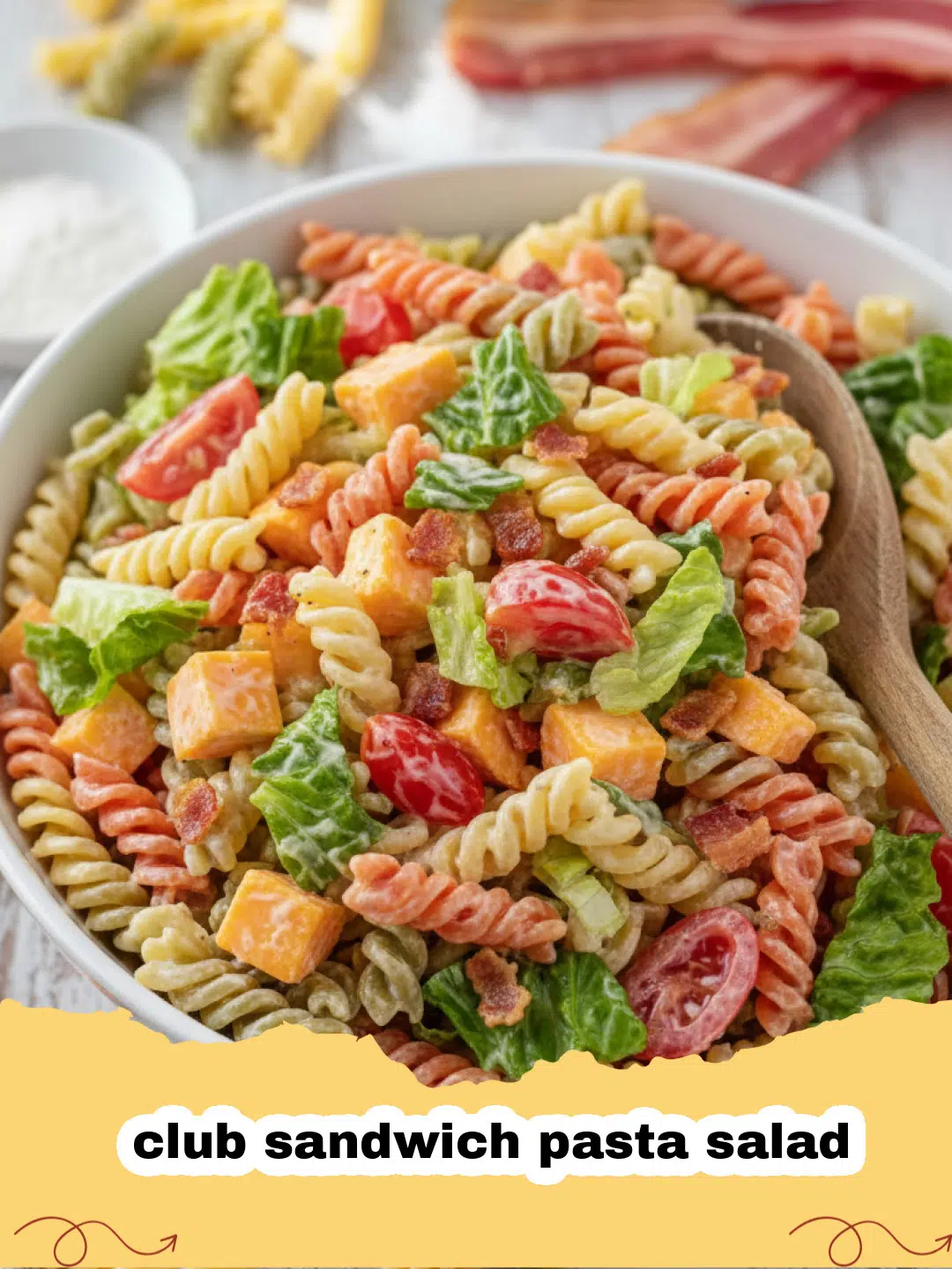 A large bowl of creamy club sandwich pasta salad with bacon, chicken, tomatoes, and lettuce on top.