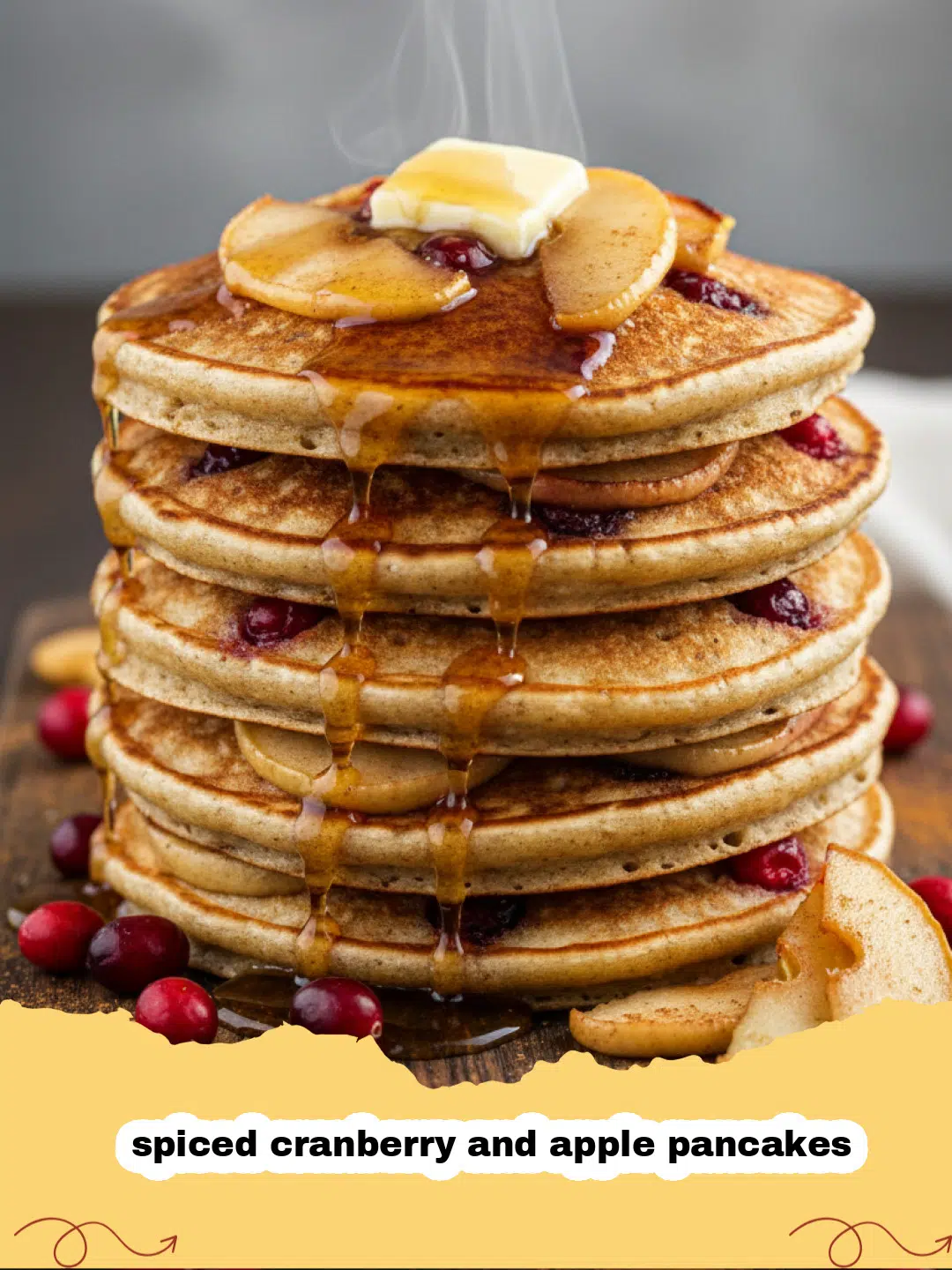 A stack of thick spiced cranberry and apple pancakes topped with maple syrup and fresh fruit.