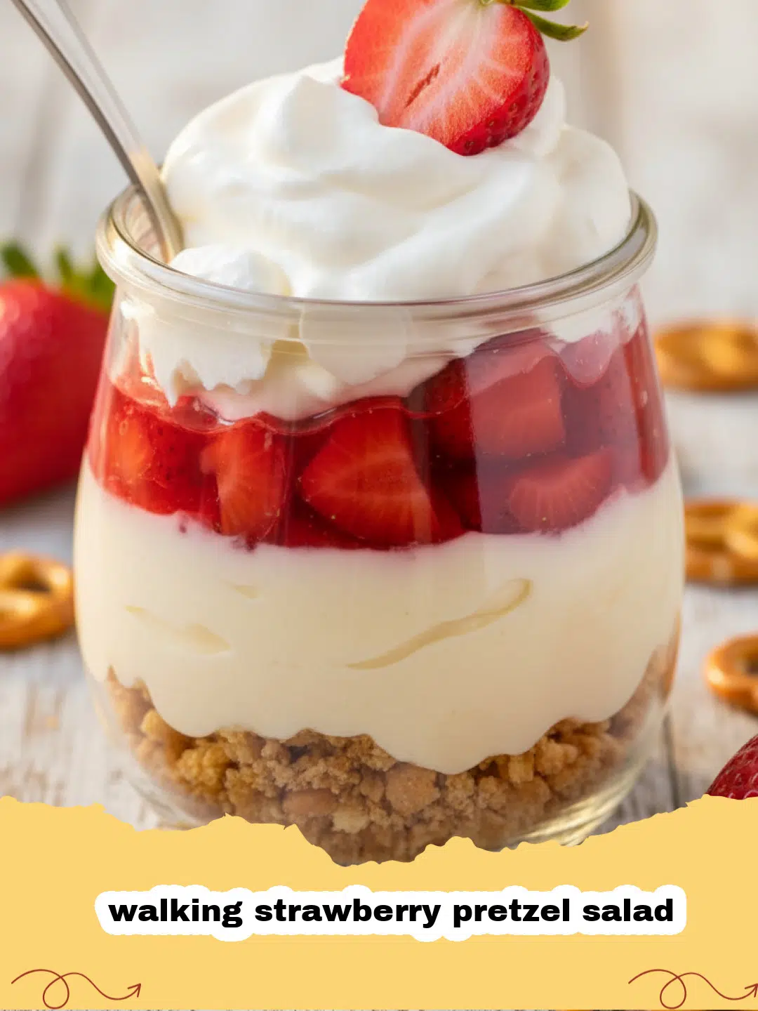 A close-up shot of individual clear cups filled with layers of crunchy pretzel crust, creamy white cream cheese filling, and bright red strawberry gelatin with fresh strawberry slices, ready to be enjoyed as a walking strawberry pretzel salad.