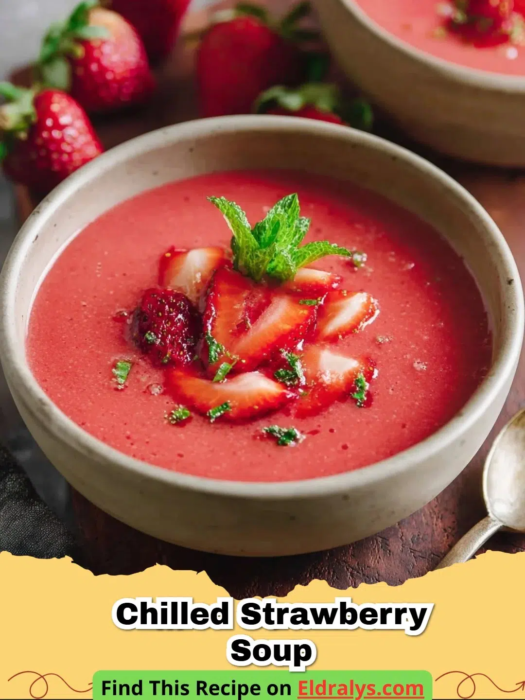 A bowl of vibrant pink Chilled Strawberry Soup garnished with mint and fresh berries.